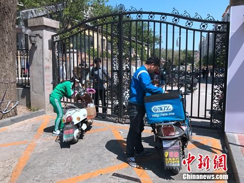 2016年4月21日，北京交通大学南门附近，由于快递电动车无法进入校园，一名学生隔着铁门取外卖。潘心怡 摄