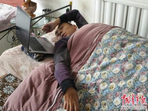 　在家中的床上，都海成手握铅笔，用笔头敲电脑键盘进行文学创作。中国青年报·中青在线记者 马富春/摄